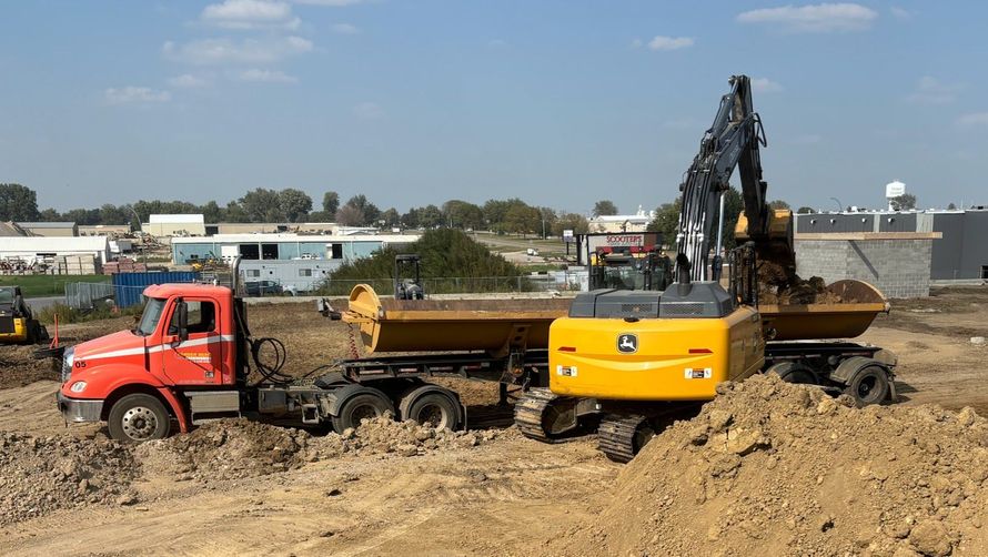 Red dump truck and yellow excavator at a dirt construction site under a clear sky