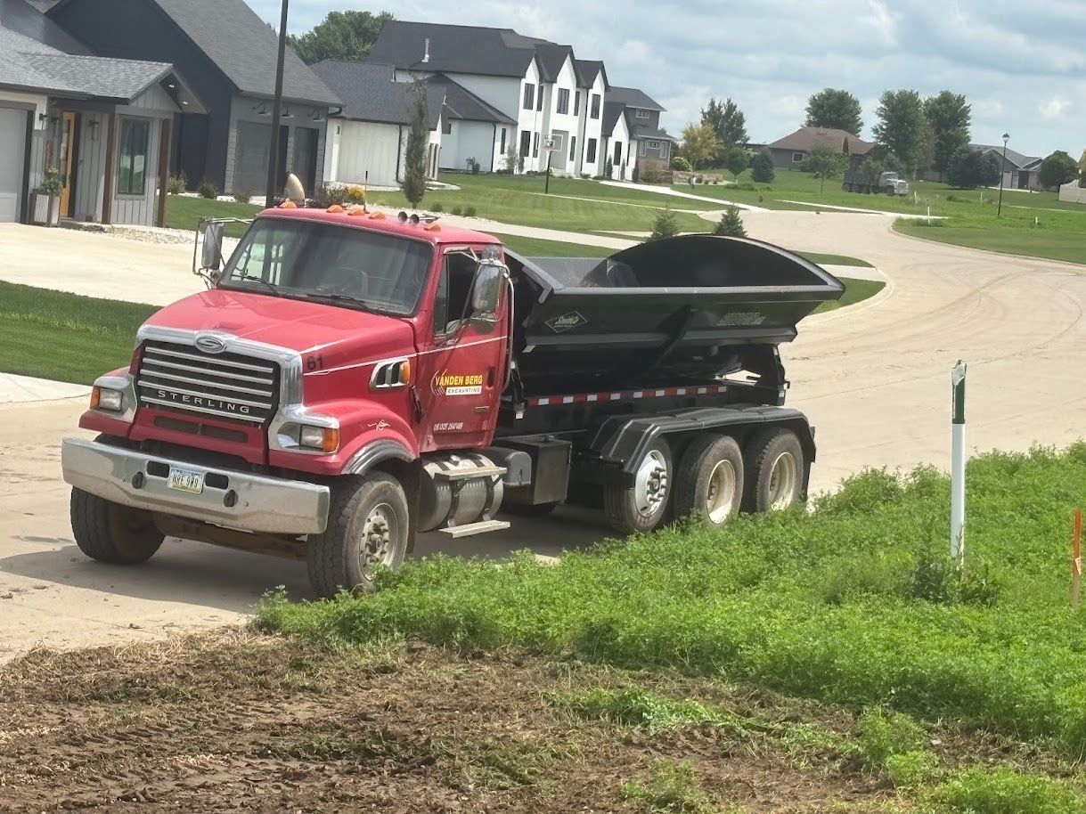 Red dump truck hauling black dirt on a suburban street near new houses