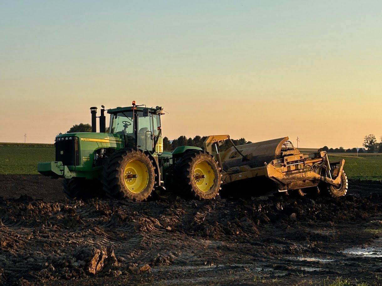 Green tractor tilling a dark field at sunset with a warm sky