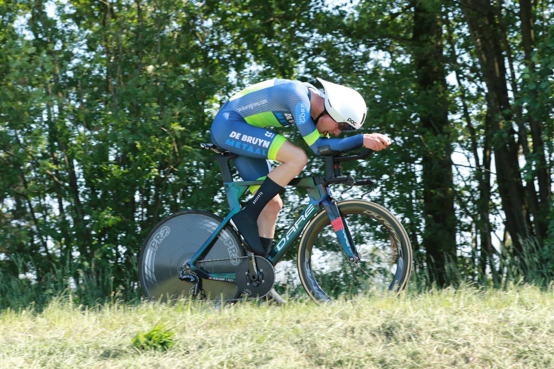 Een wielrenner in een blauw-groen uniform rijdt op een tijdritfiets over een graspad.