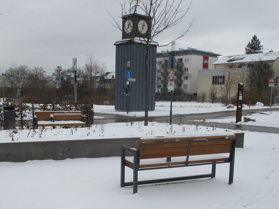 Ein verschneiter Park mit einer Bank und einer Uhr im Hintergrund
