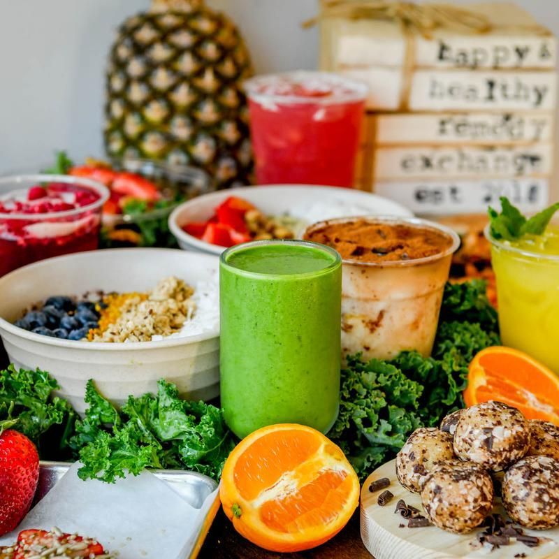 Colorful healthy breakfast spread with smoothies, fruit, granola, and kale on a table.