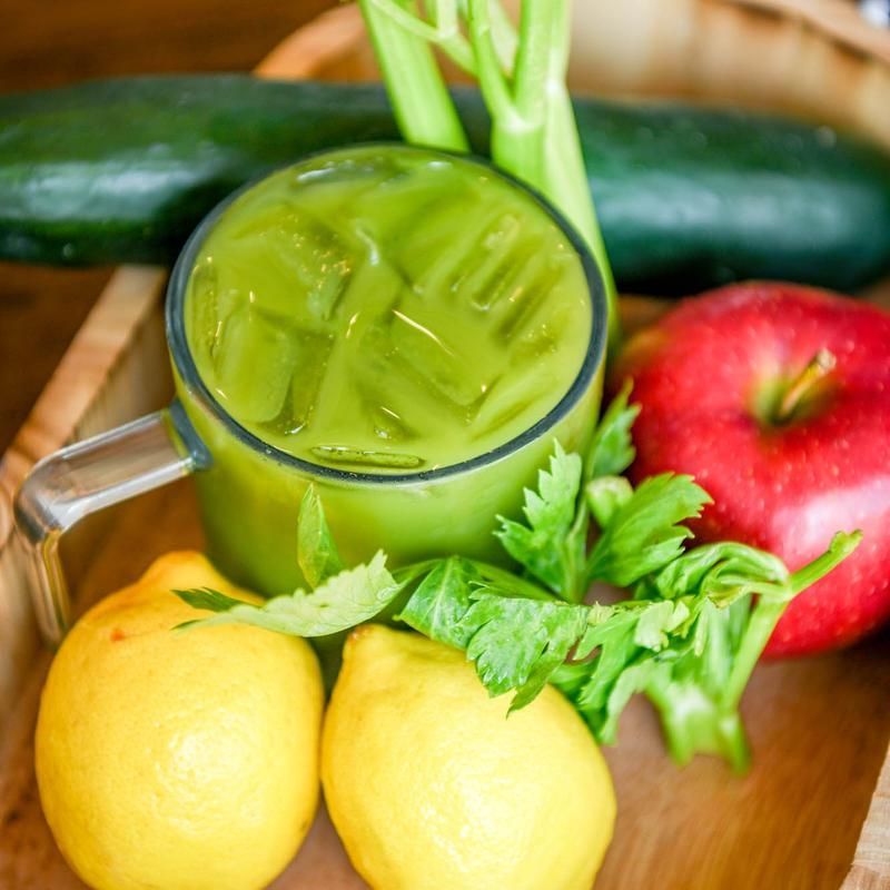 Fresh green juice in a glass with lemons, apple, cucumber, and parsley on a wooden tray