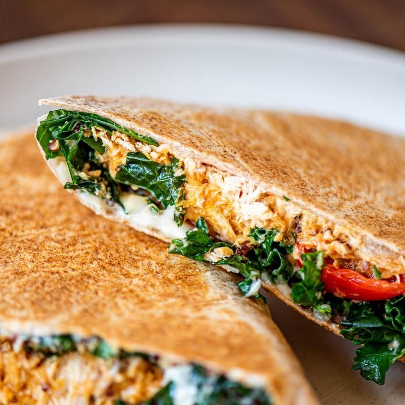 Grilled wrap cut in half, showing spinach, tomato, and creamy filling on a white plate
