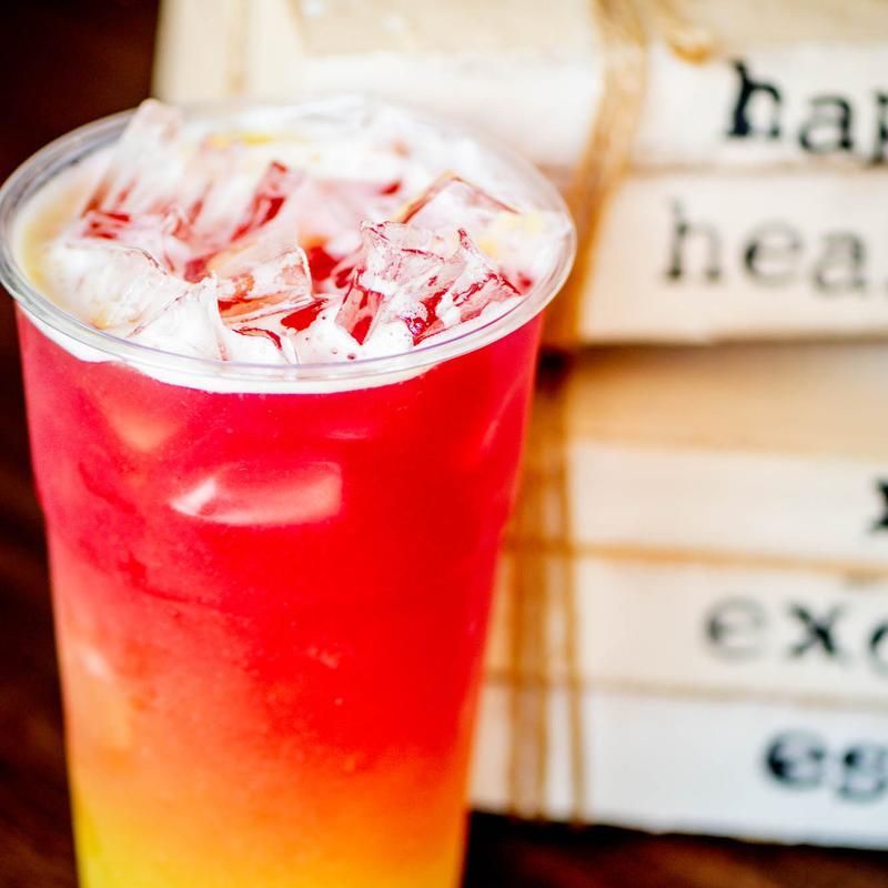 Colorful iced red drink in a clear glass, with ice cubes and a yellow-orange layer at the bottom.