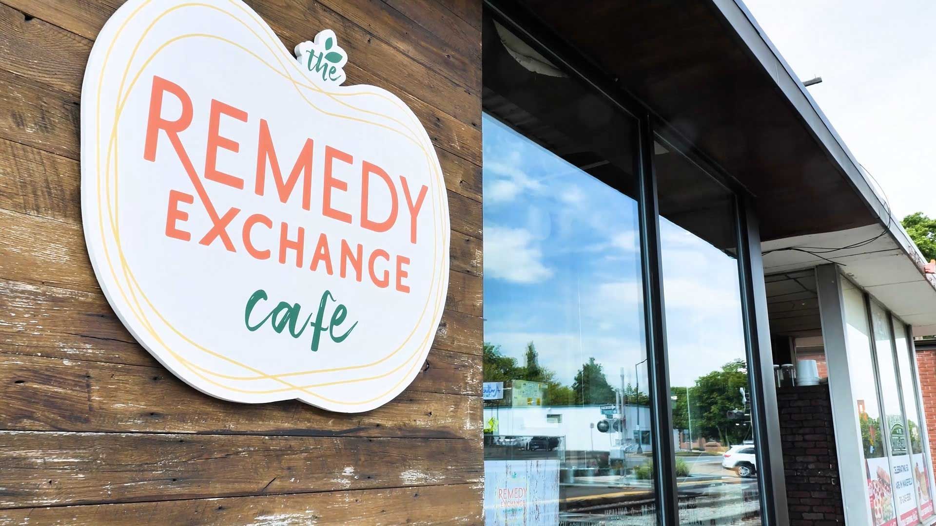 Remedy Exchange Cafe sign on a rustic wooden wall beside large windows.