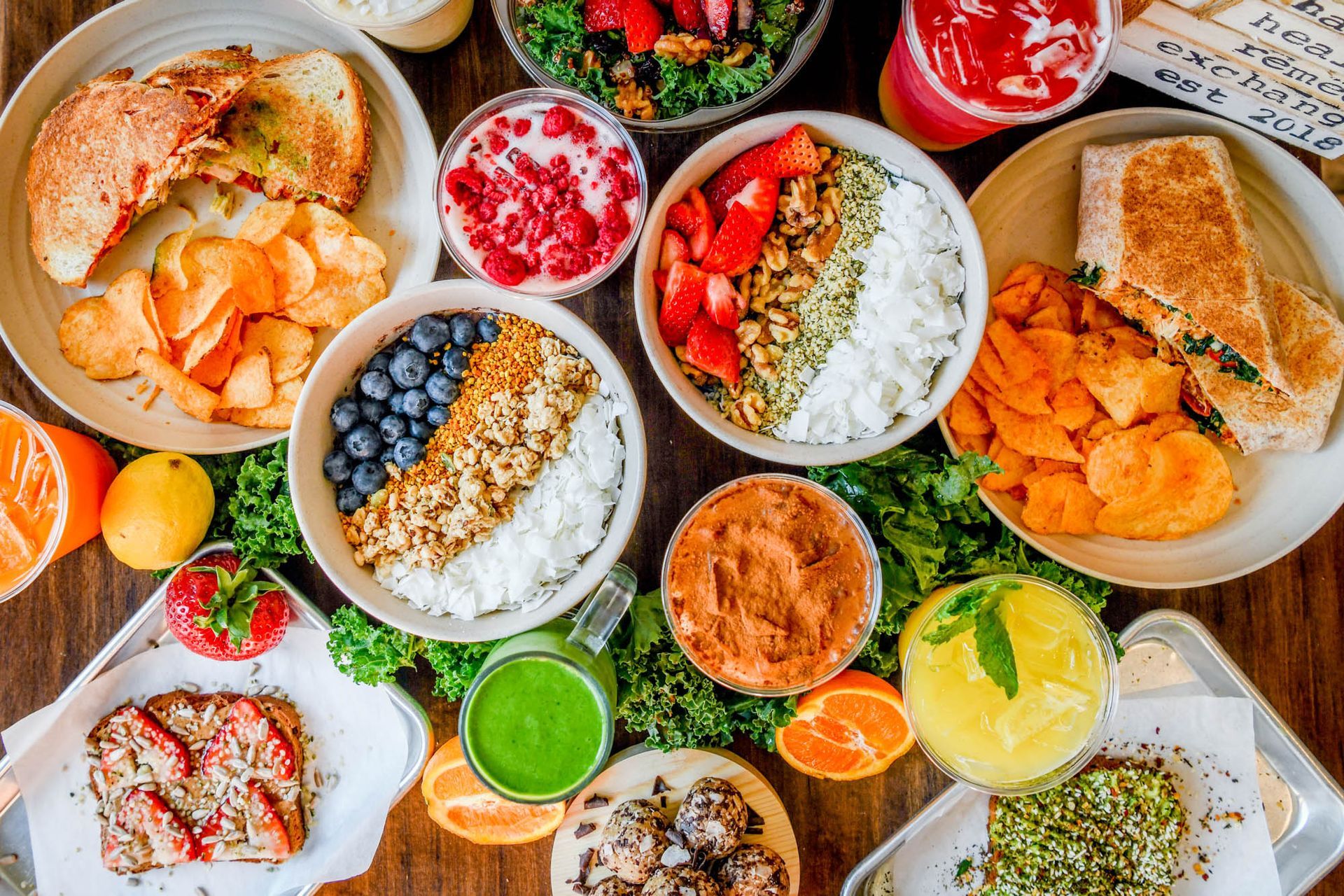 Assorted colorful bowls of breakfast foods, fruit, and dips arranged on a table in a vibrant overhead spread