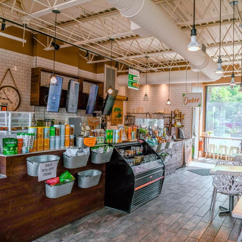 Bright café interior with coffee display, grinders, and a pastry case by large windows.