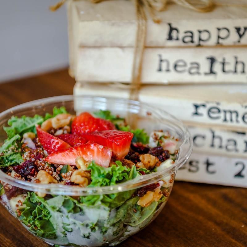 Strawberry-topped salad in a glass bowl beside stacked rustic books on a wooden table