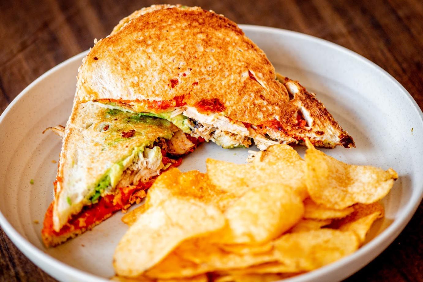 Grilled sandwich on a plate with potato chips, cut in half to show filling