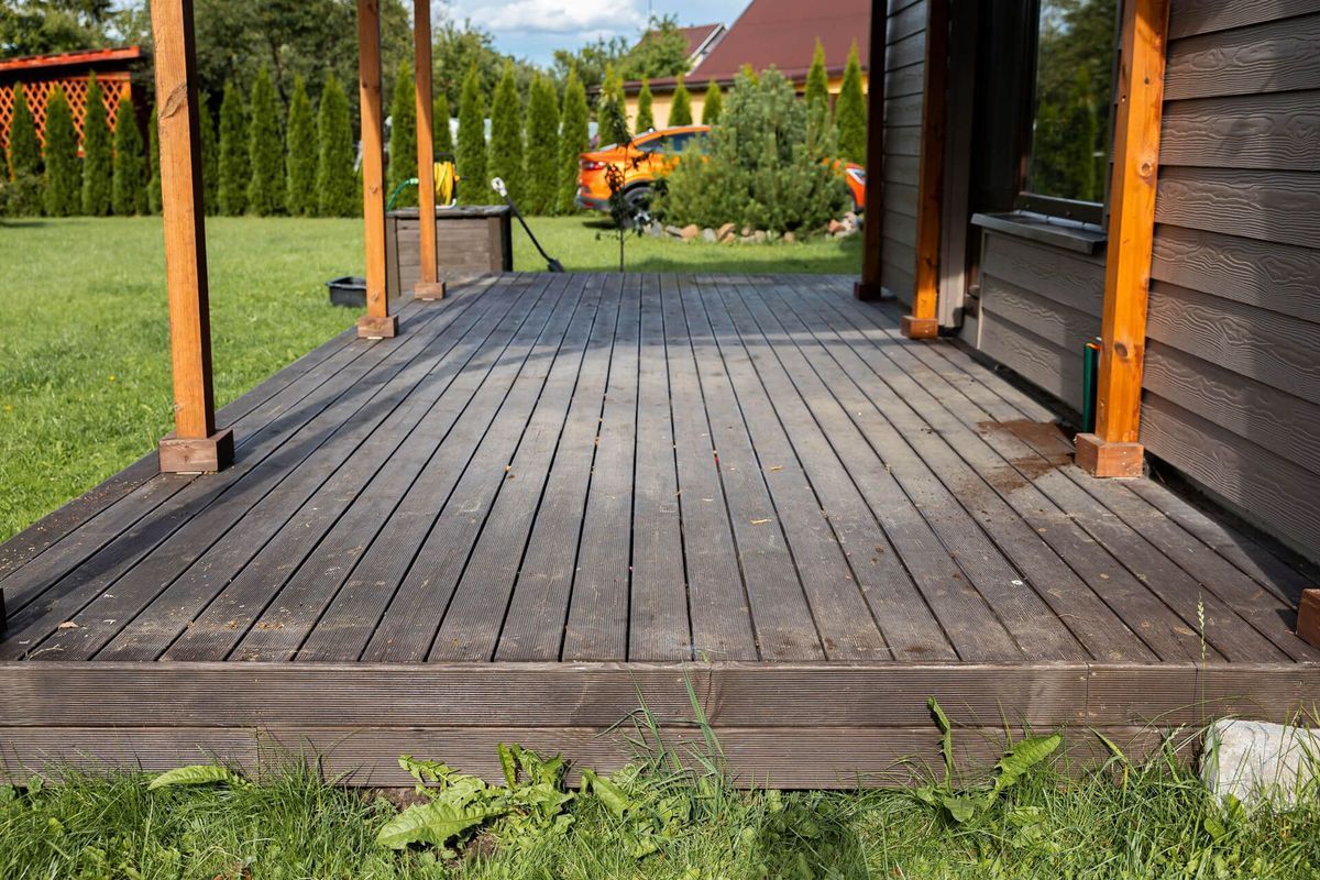 Wooden porch with dark planks, orange posts, and a grassy yard in the background