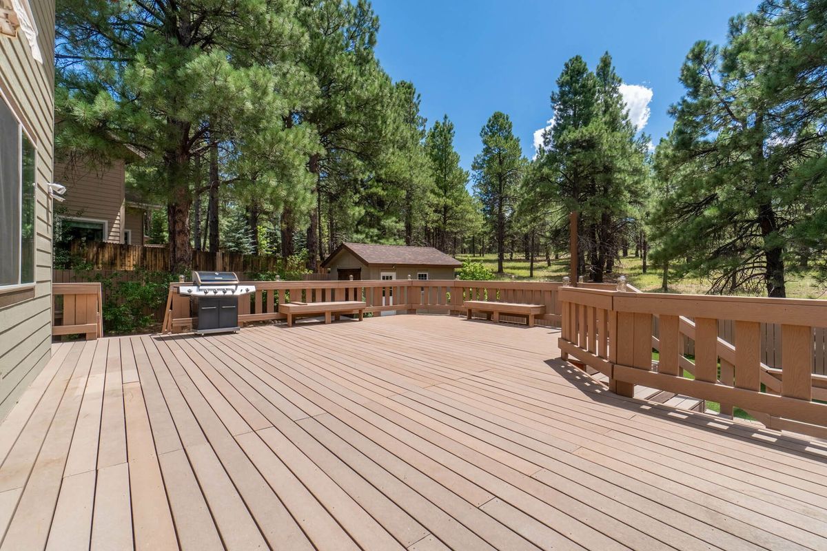 Spacious wooden deck overlooking pine trees and a small cabin under a clear blue sky