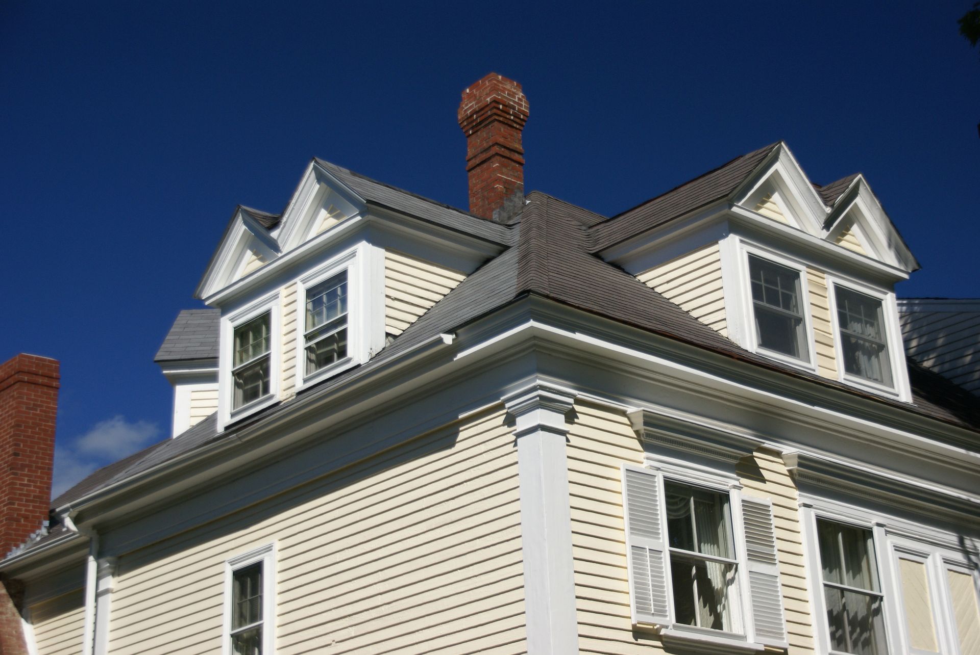 White house roofline with dormer windows and a brick chimney against a clear blue sky