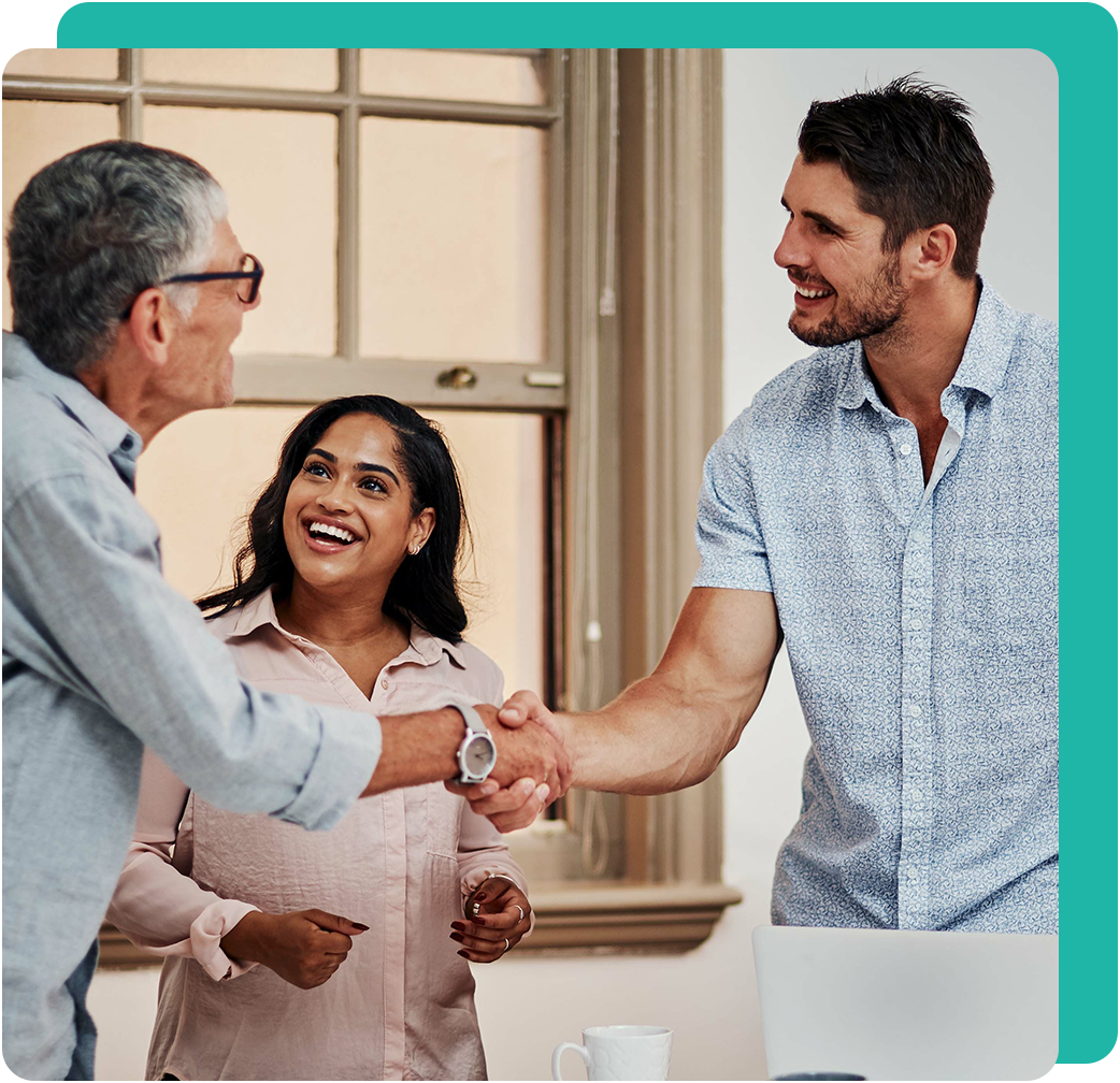 Three people in office. A man shakes hands with another man, woman smiles.