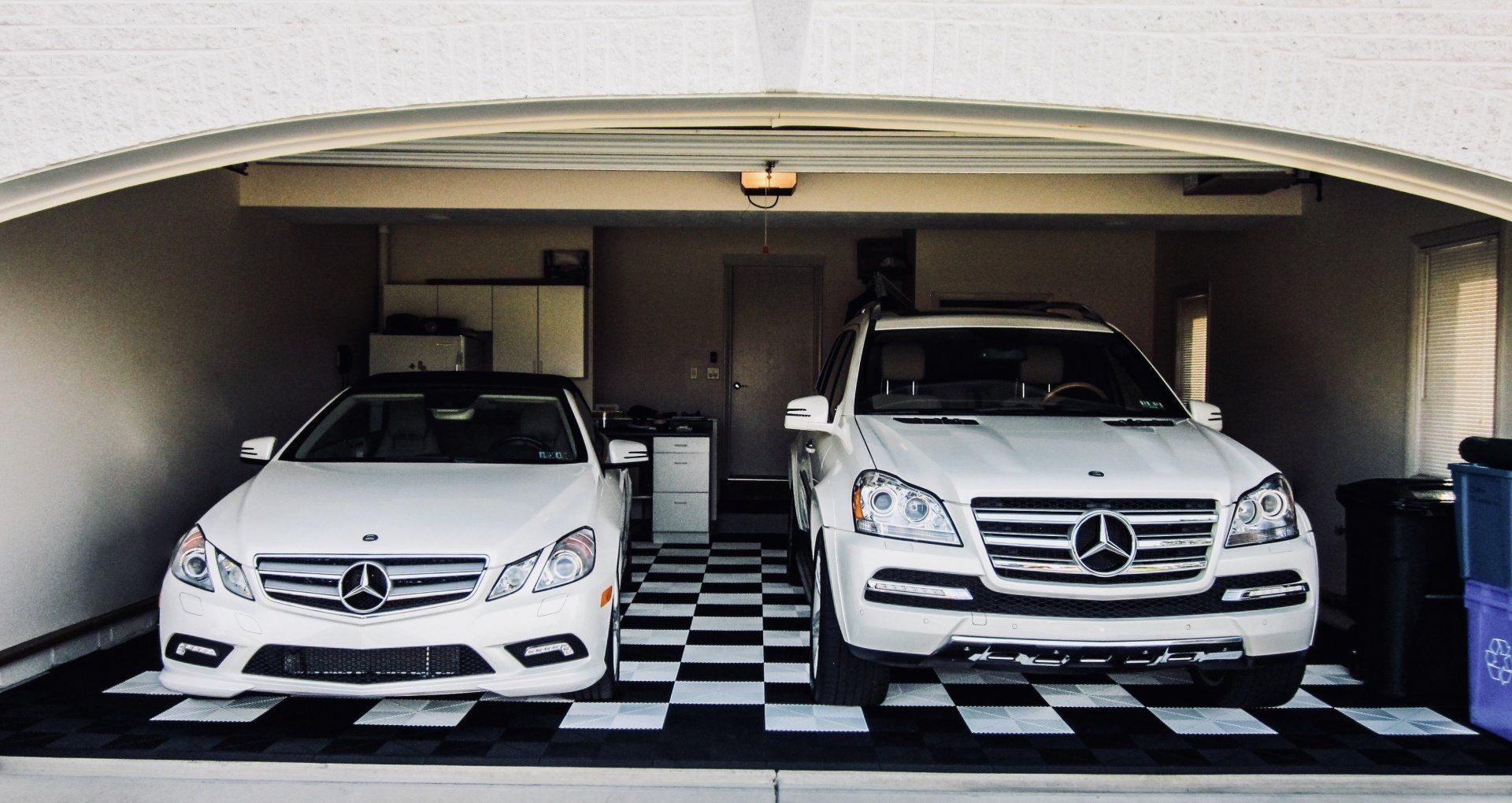 two white cars are parked in a garage with a Swisstrax floor .