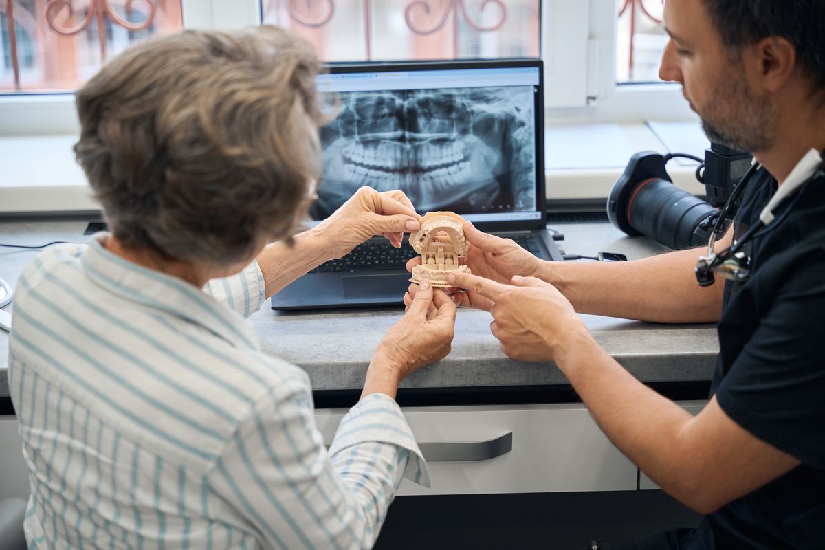 Dentist showing a jaw X-ray and dental model to a patient at a desk