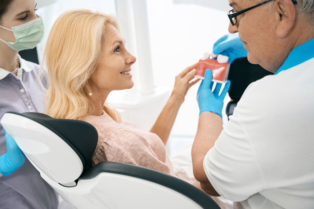Change your life with dental implants from our family dentist in Longmont, CO. woman smiling at dentist holding dental implants