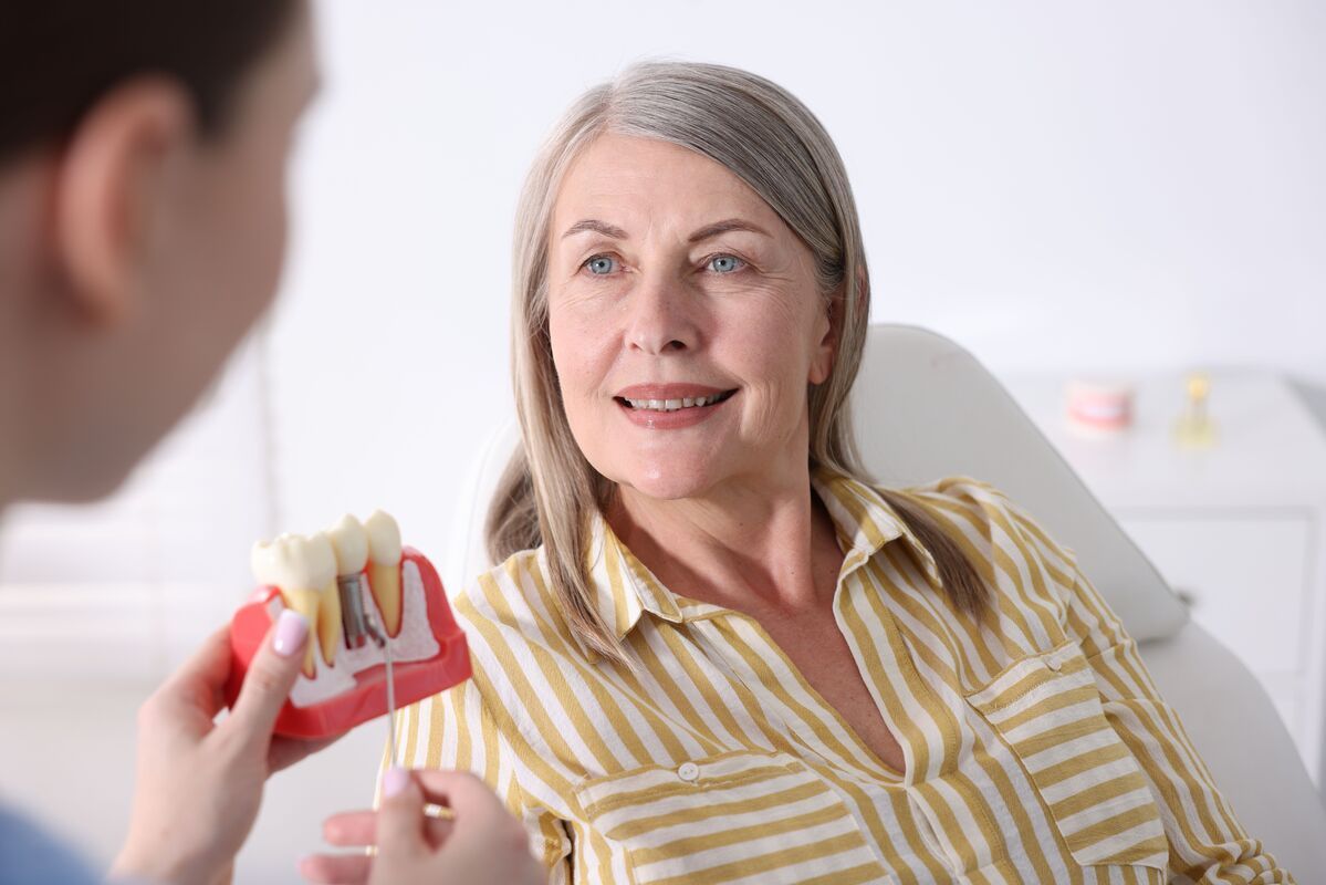 Dentist showing a model of teeth to a smiling patient in a bright clinic