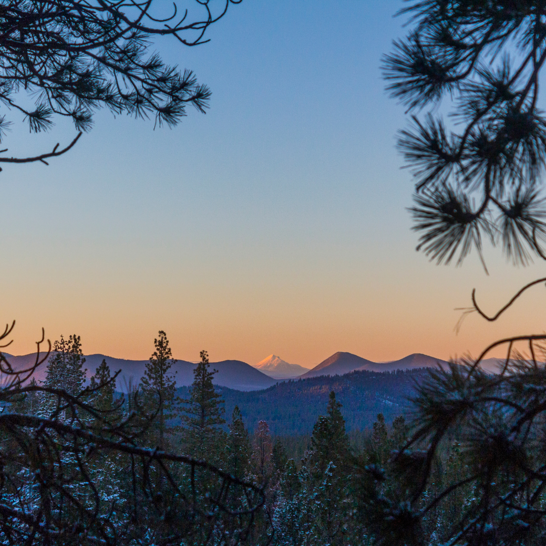 A sunset over a mountain range with trees in the foreground
