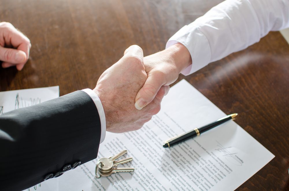 Two People Shaking Hands Over a Contract With a Pen and Keys on a Table — Property Transfer Professionals In Wyong, NSW