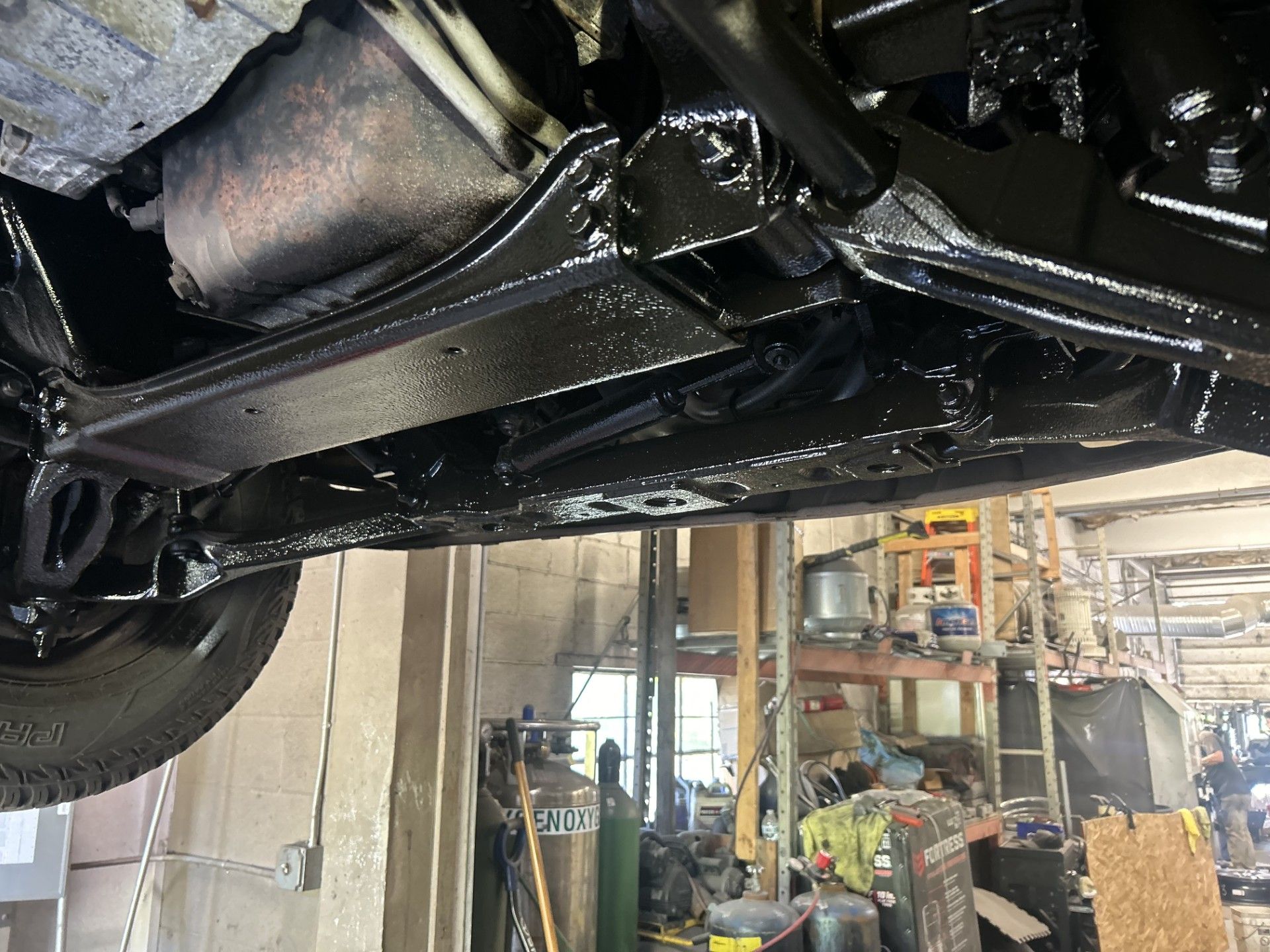 Car painter in protective clothes and mask painting automobile bumper with metallic paint and varnish in chamber workshop.