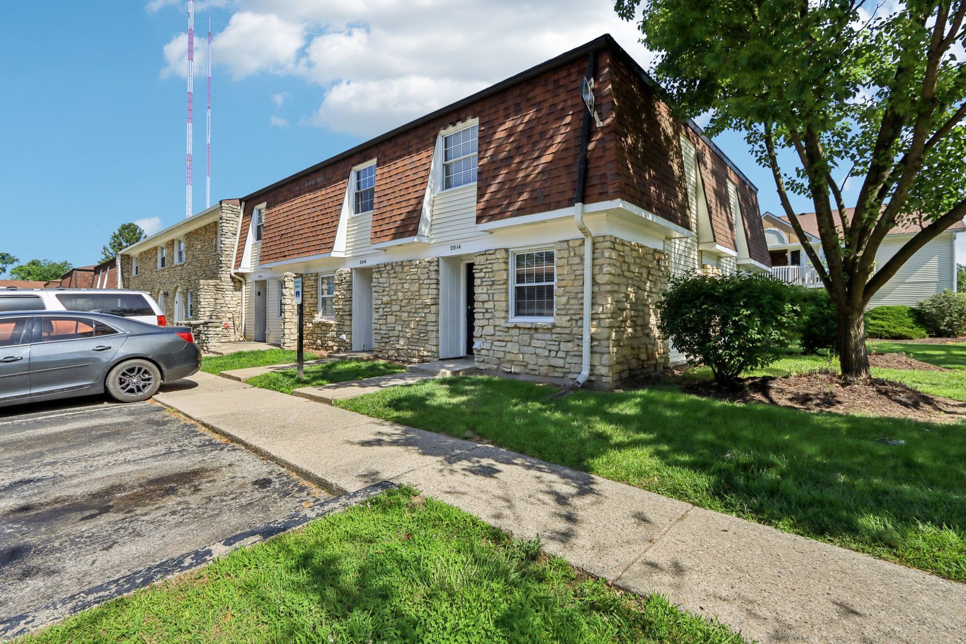 Townhouses with brick roofs, stone facade, and a sidewalk in front, with parked cars.