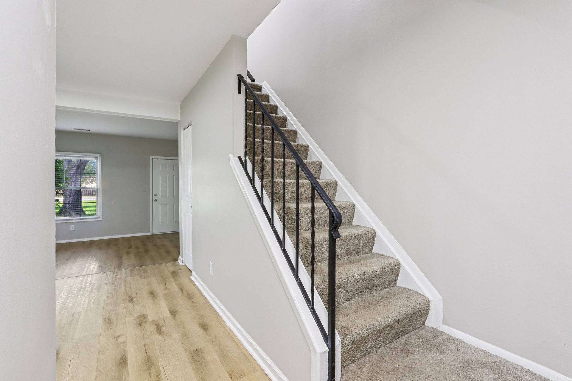 Interior hallway with stairs on the right, light wood floors, and a doorway leading to a room with a window.