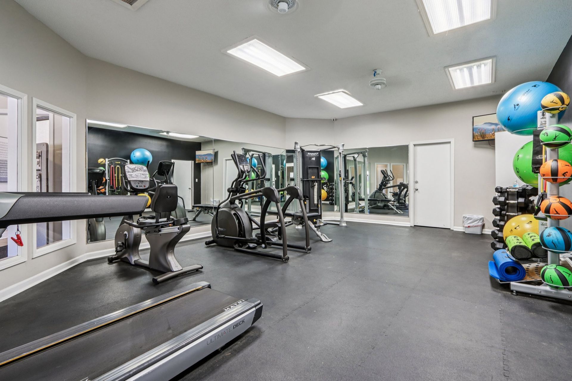 Gym interior with treadmill, elliptical, weight machines, mirrors, and exercise balls.