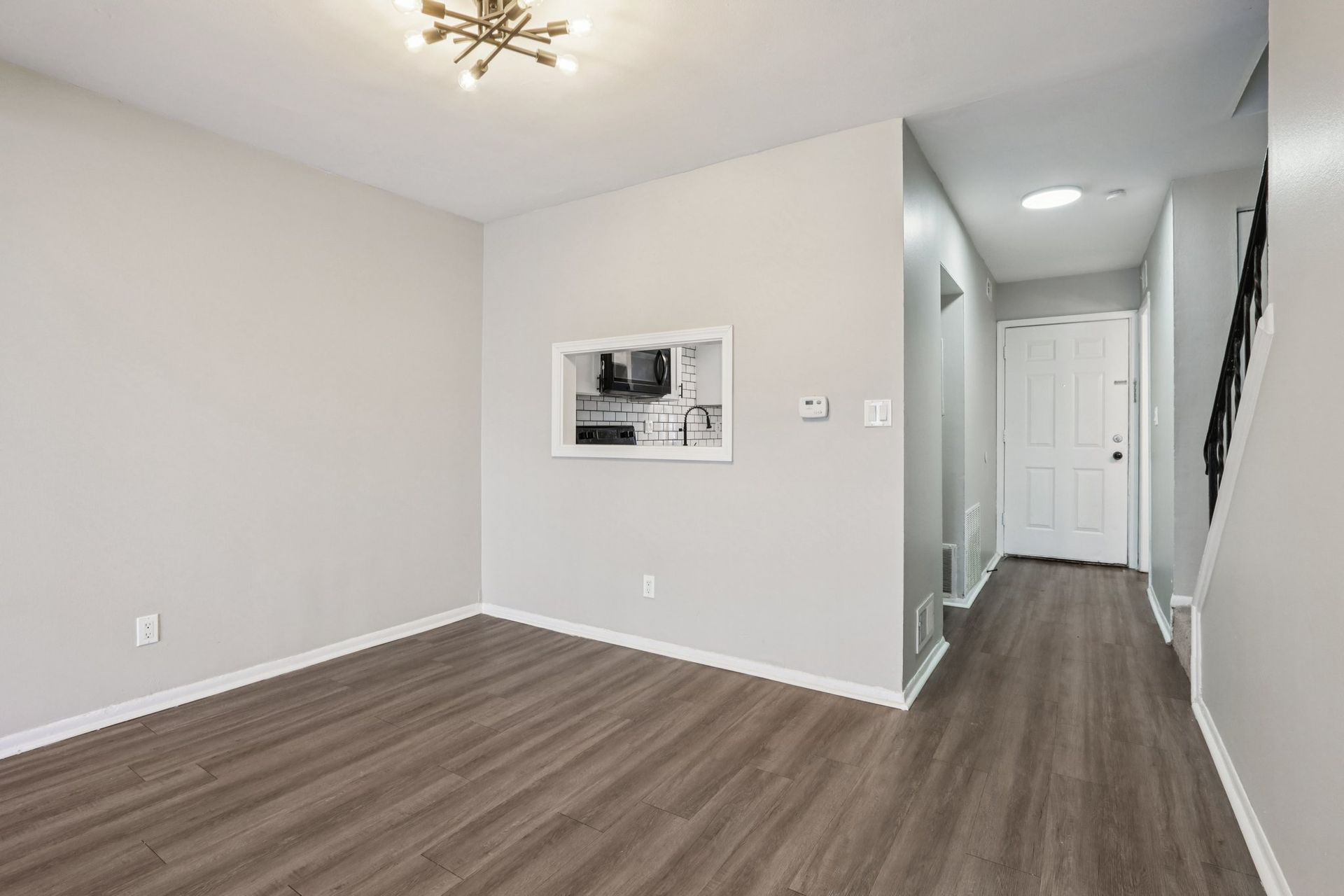 Empty room with gray walls, wood floors, and a hallway leading to a white door.