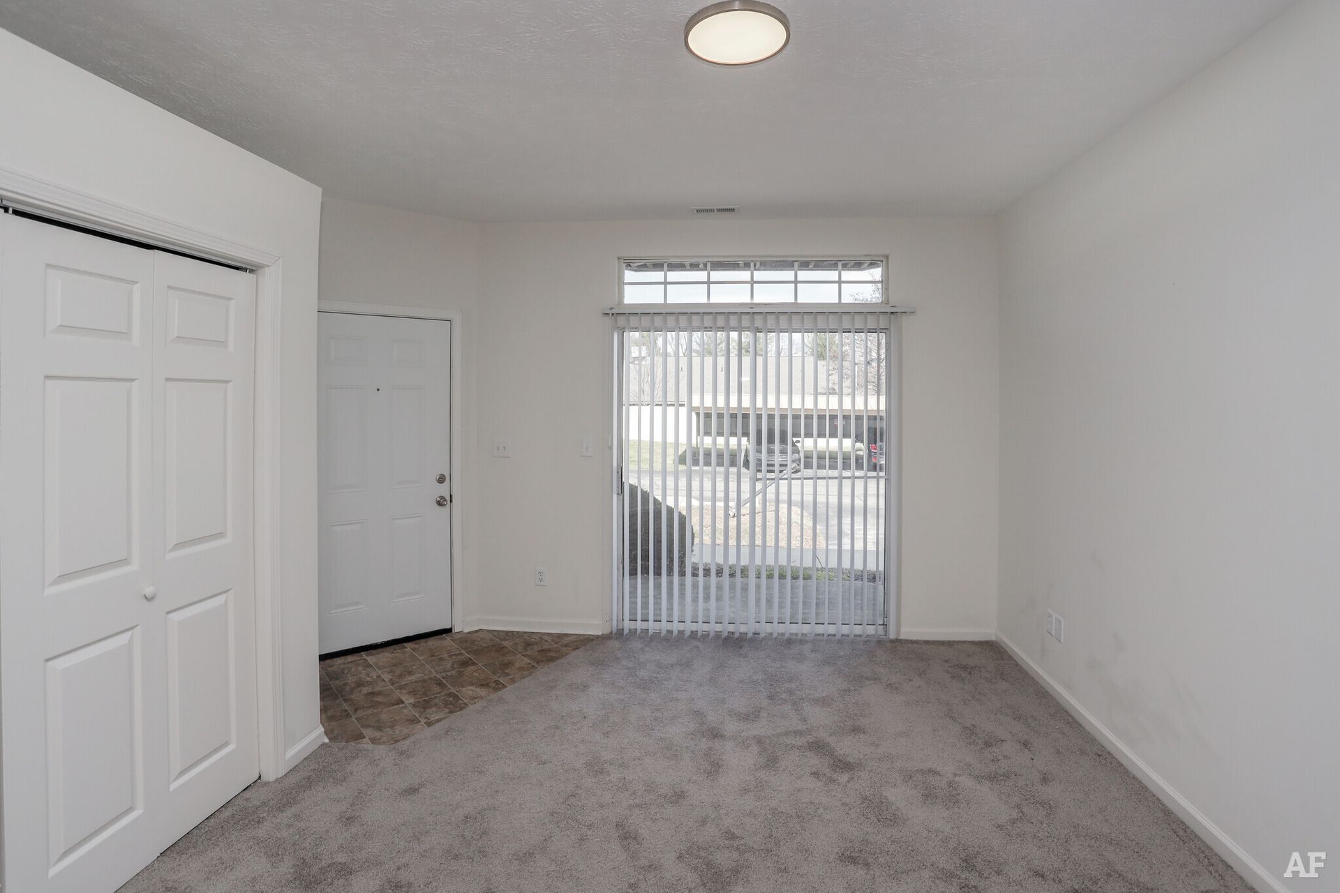 Empty room with a sliding glass door, white walls, closet, and gray carpet.