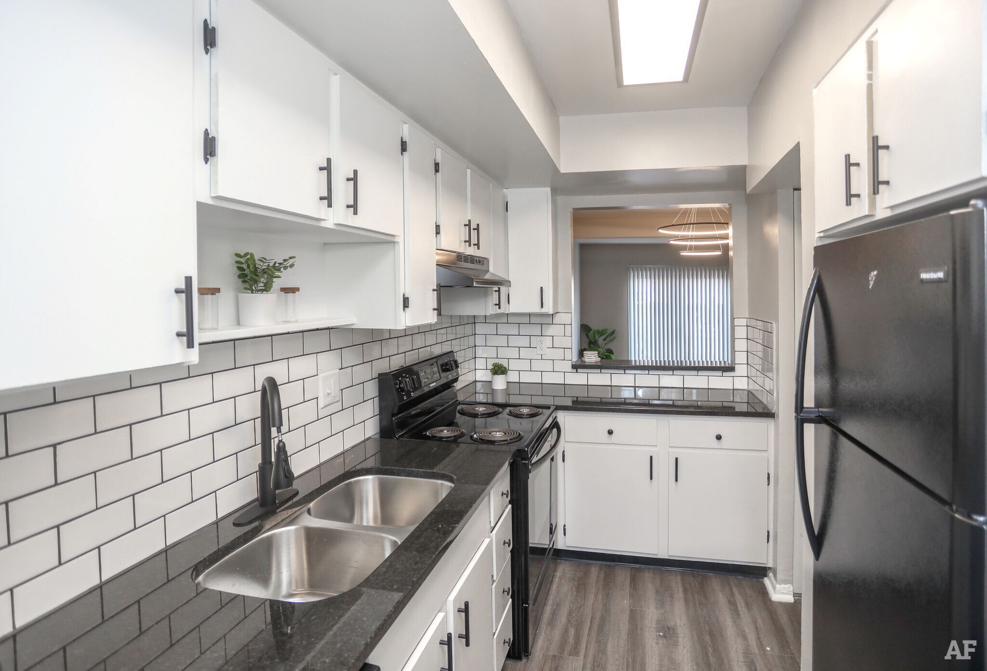 Black and white kitchen with brick-style backsplash, black appliances, and white cabinets.
