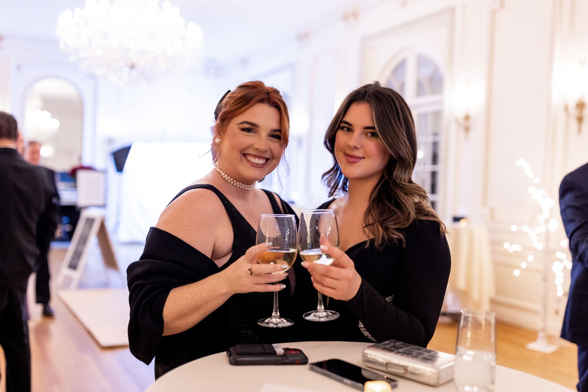 two women smiling cheering with wine glasses, at a holiday event
