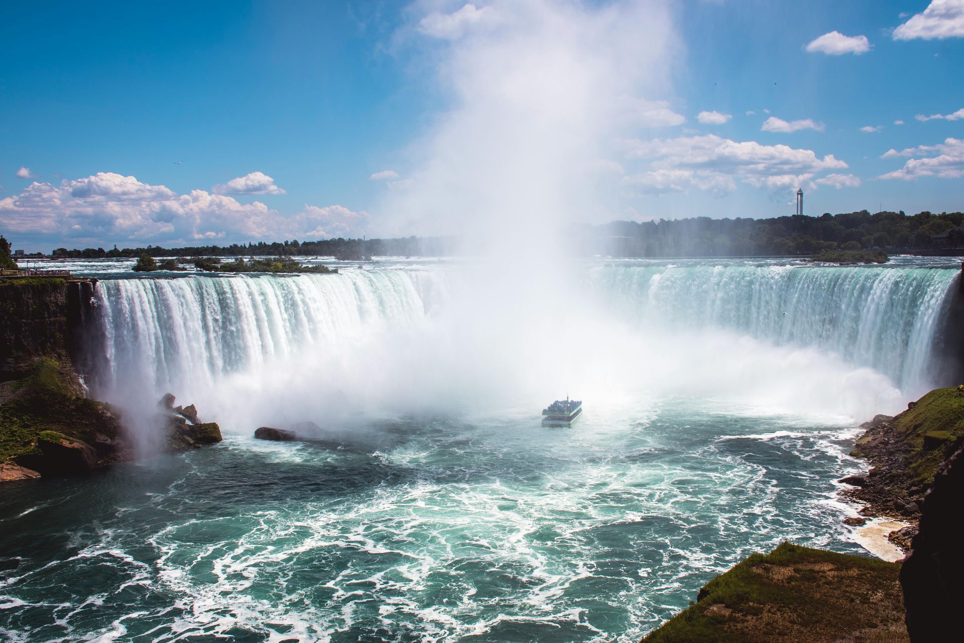 Wide waterfall plunging into a turquoise pool, with mist rising under a bright blue sky