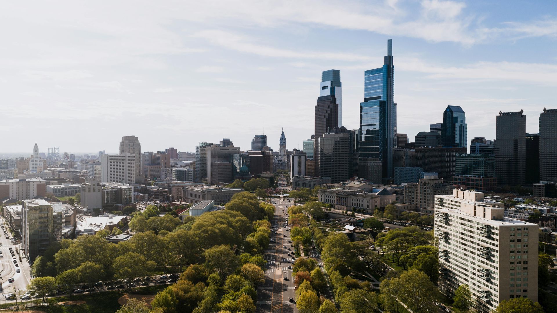 City skyline with tall modern skyscrapers above a tree-lined street on a hazy day