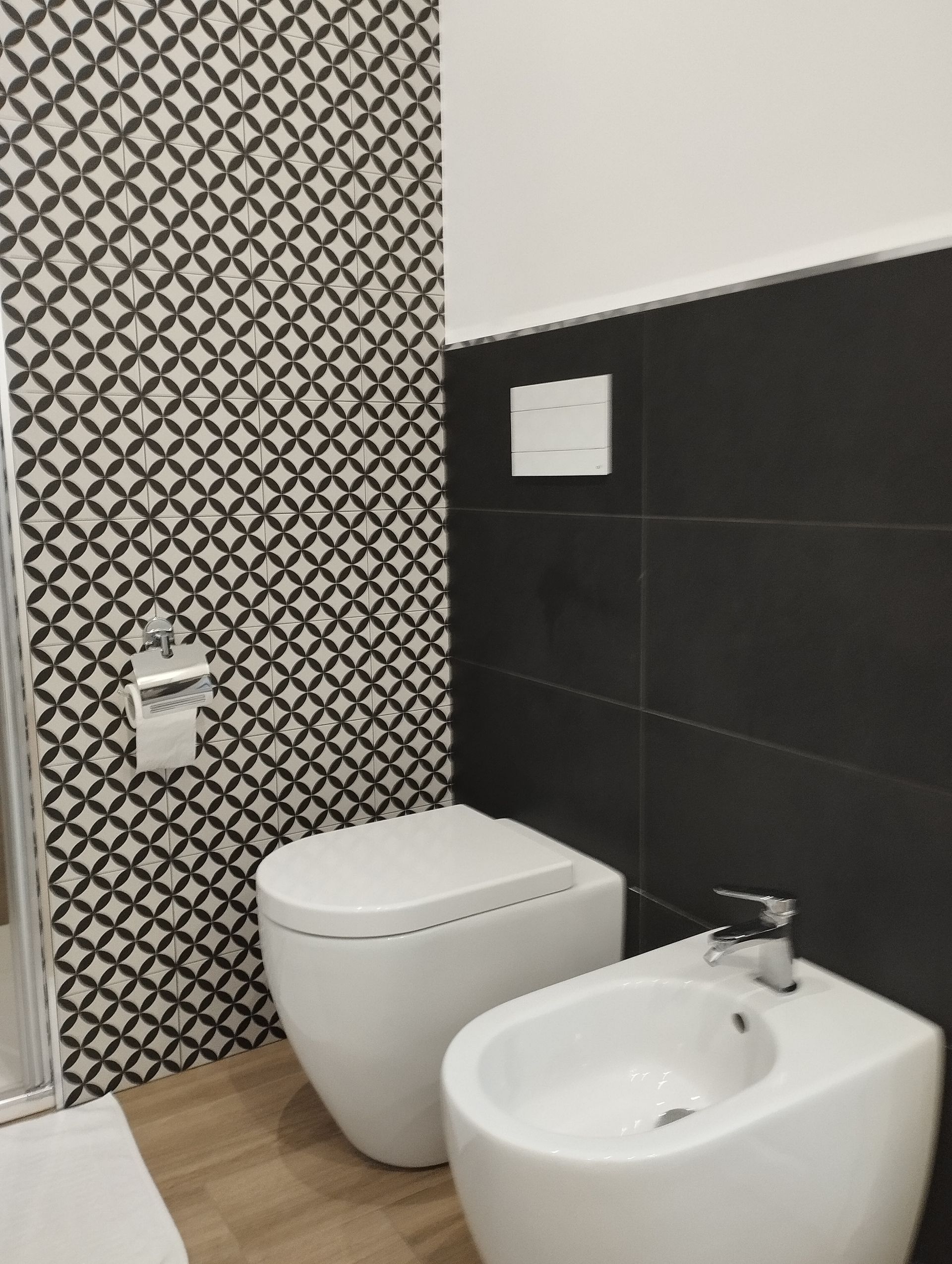 Bagno con parete piastrellata a motivi geometrici, WC e bidet. Combinazione di colori bianco e nero.