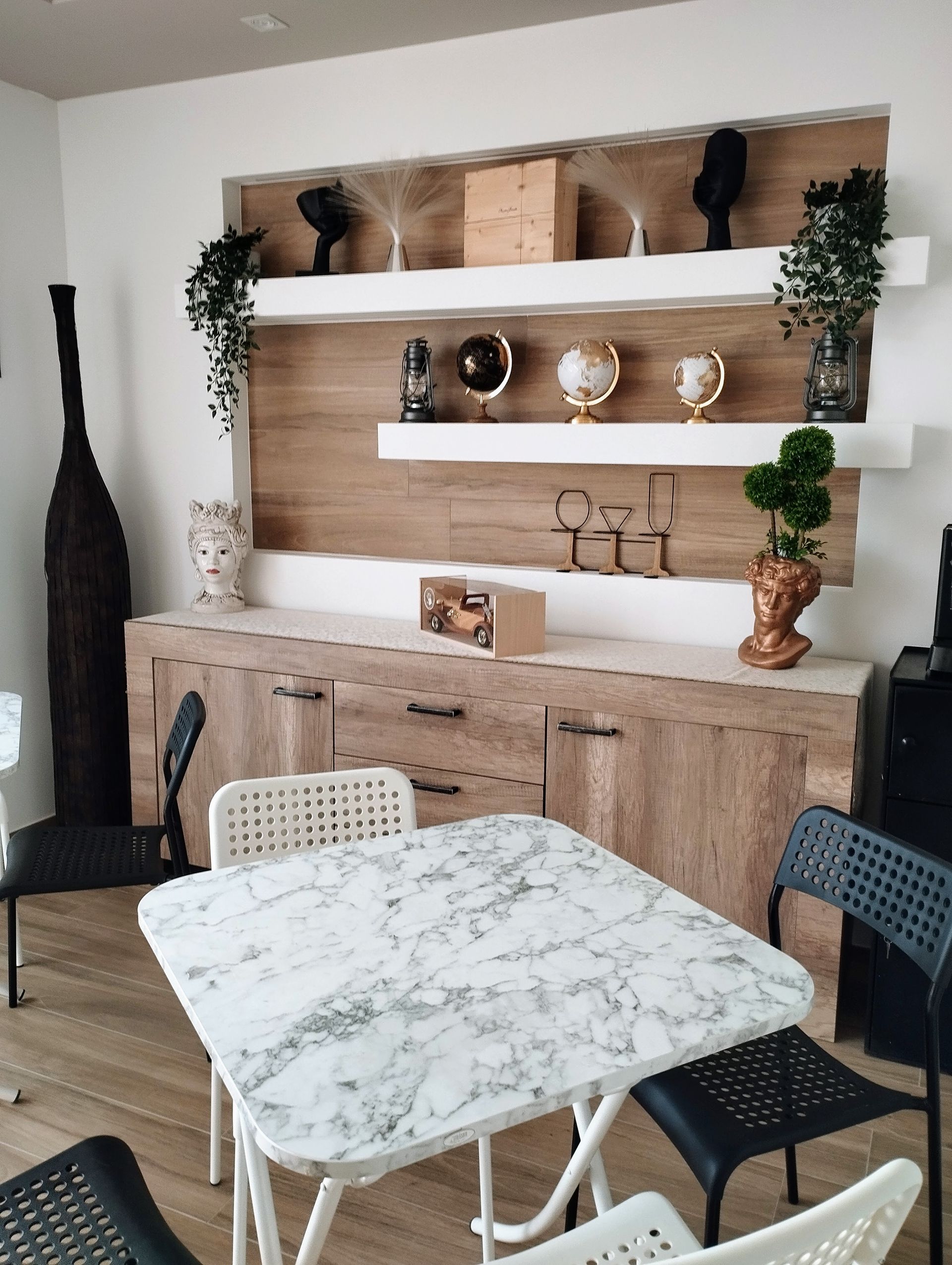 Soggiorno con tavolo in marmo, mobile in legno, scaffali decorati e sedie bianche e nere.