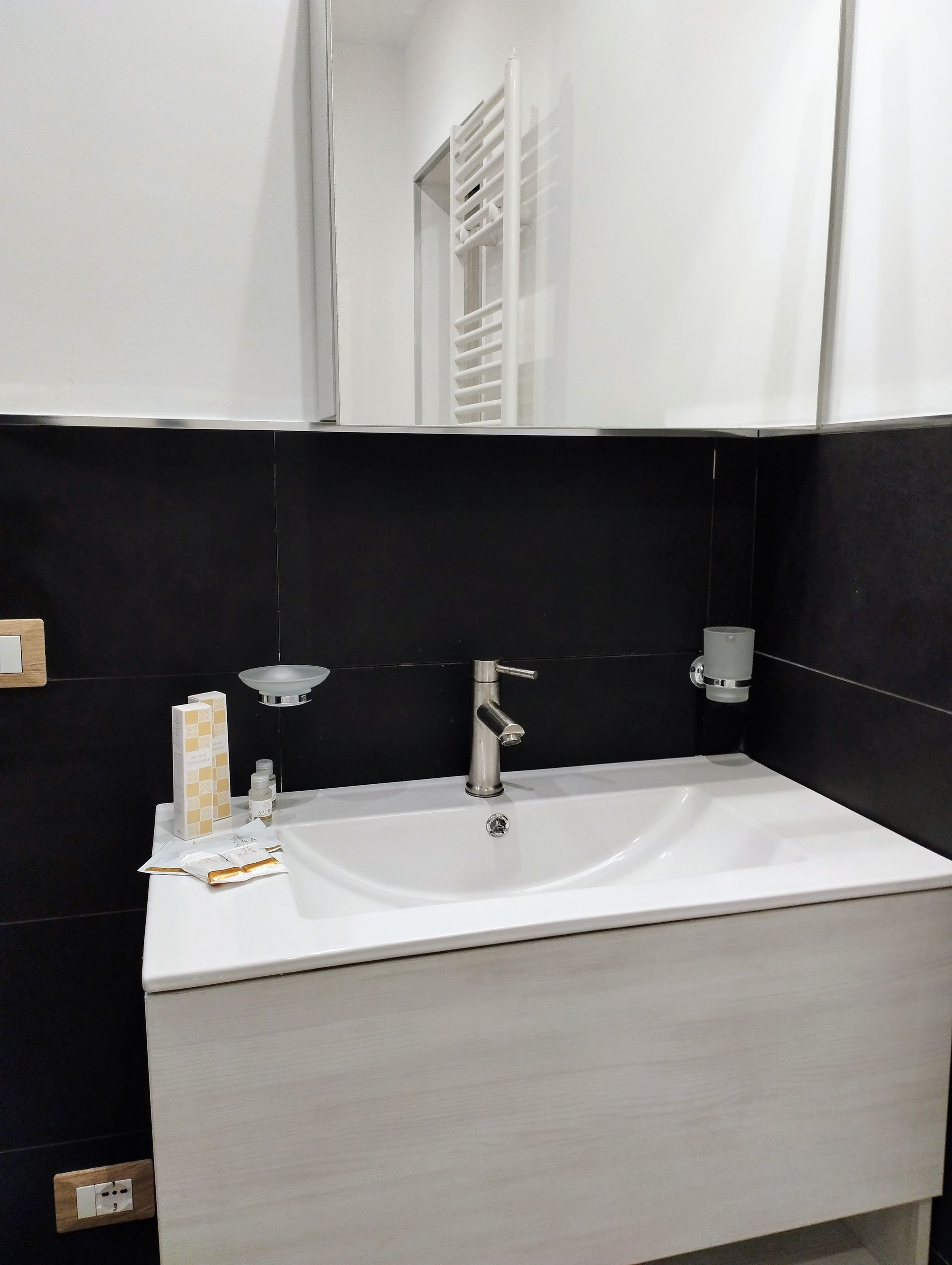 Lavandino del bagno con lavabo in porcellana bianca, rubinetto cromato, parete nera e grande specchio.