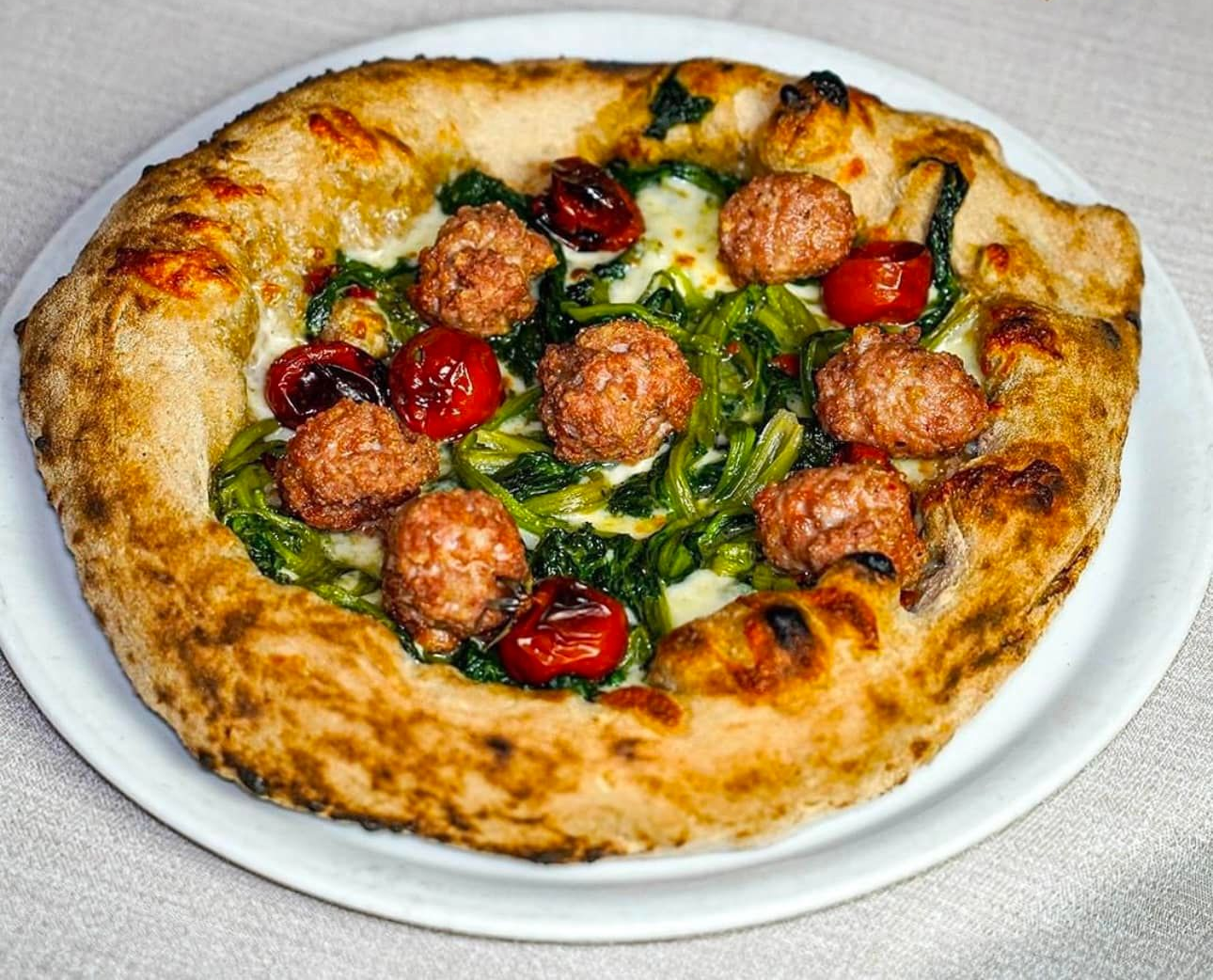 Pizza con salsiccia, spinaci e pomodori su un piatto bianco.