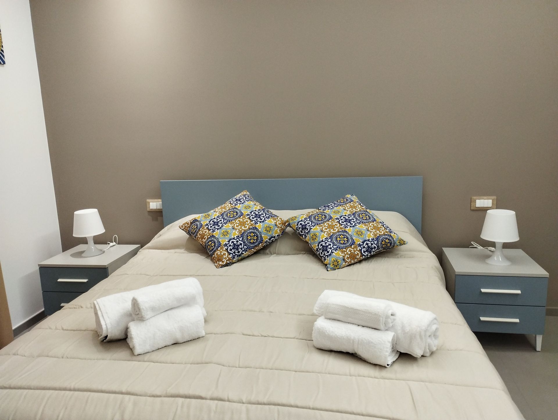 Camera da letto con letto matrimoniale, testiera azzurra, comodini, lampade e asciugamani.