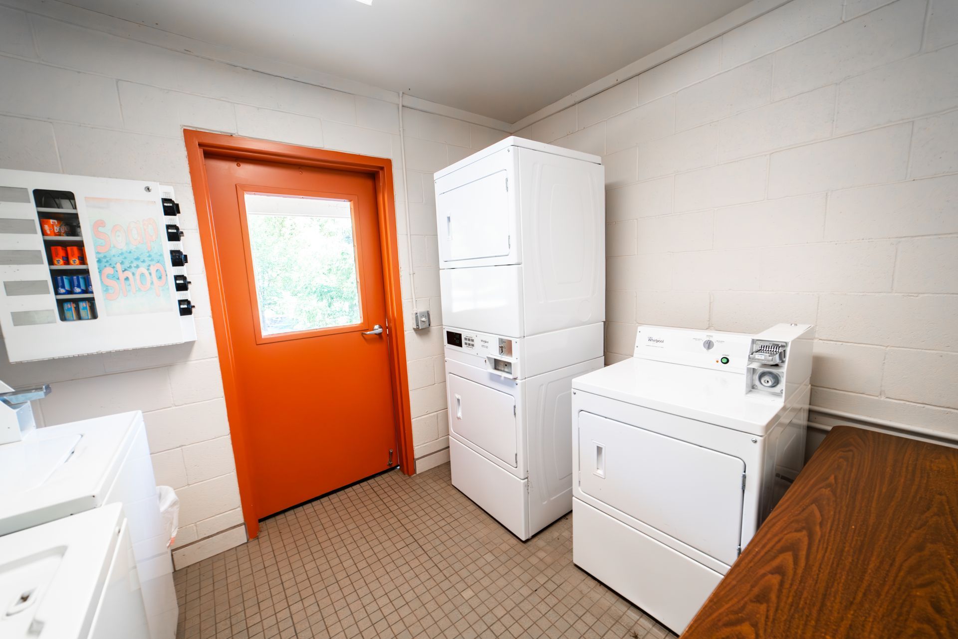 Laundry room with white appliances, an orange door, and a vending machine.