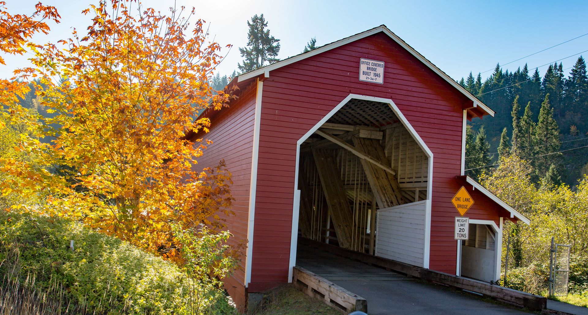 Red covered bridge with white trim surrounded by autumn trees in a rural forest setting