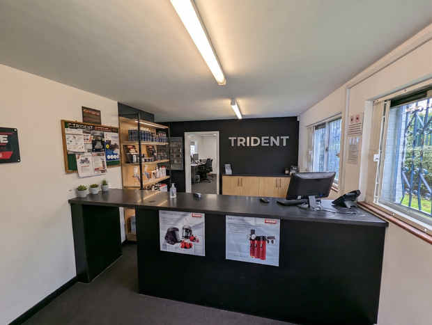 Trident reception desk in a small office with black counter, shelves, posters, and bright windows.