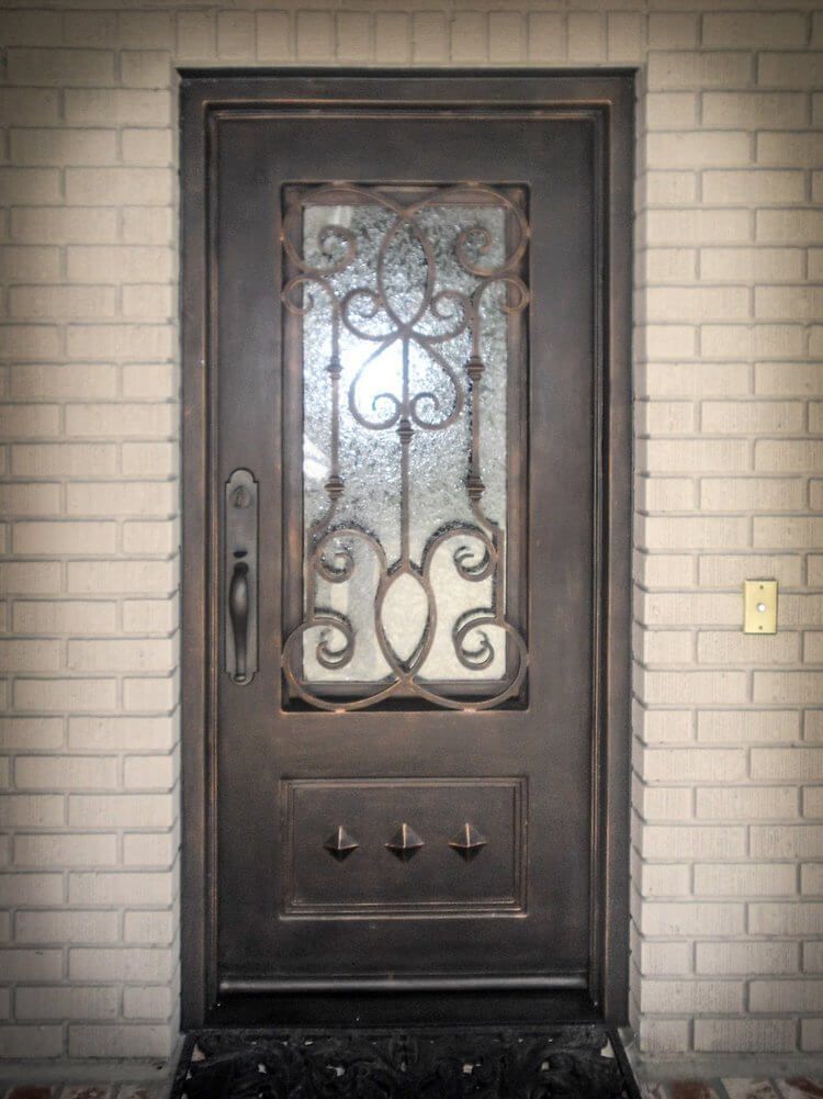 A wrought iron door with a glass window is on a white brick wall.