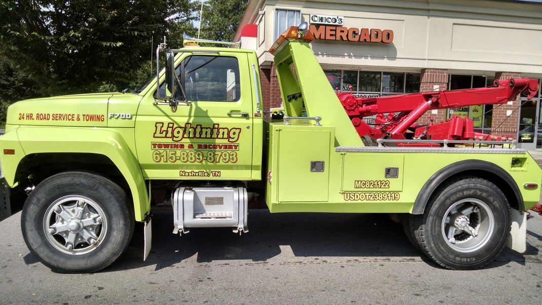 A yellow tow truck is parked in front of a store called lightning