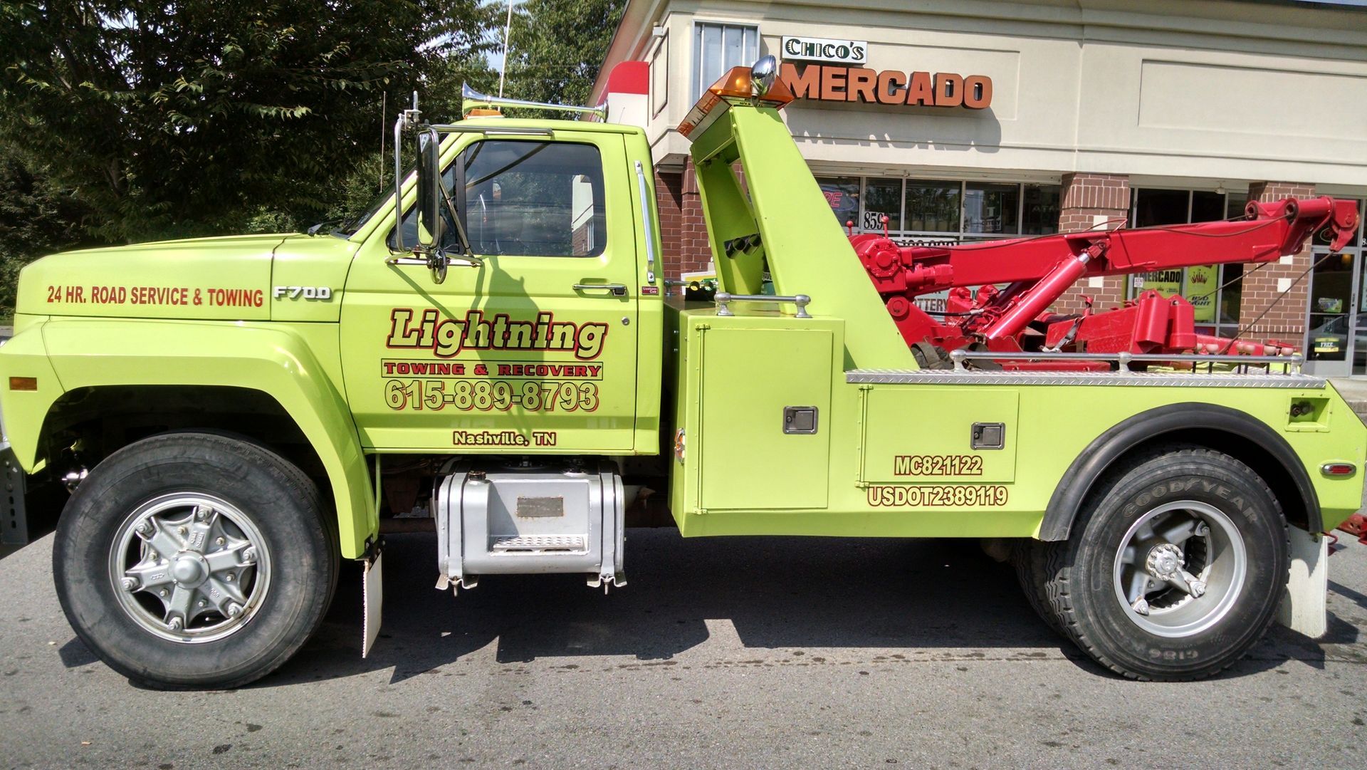 A yellow tow truck is parked in front of a store called lightning