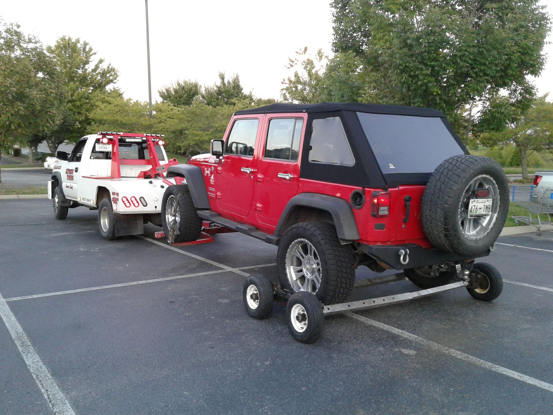 A red jeep is being towed by a white tow truck