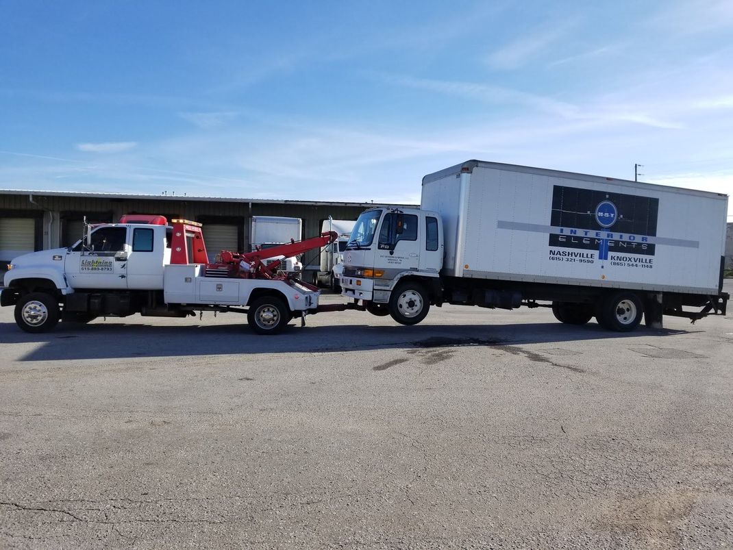 A tow truck is towing a large white truck in a parking lot.