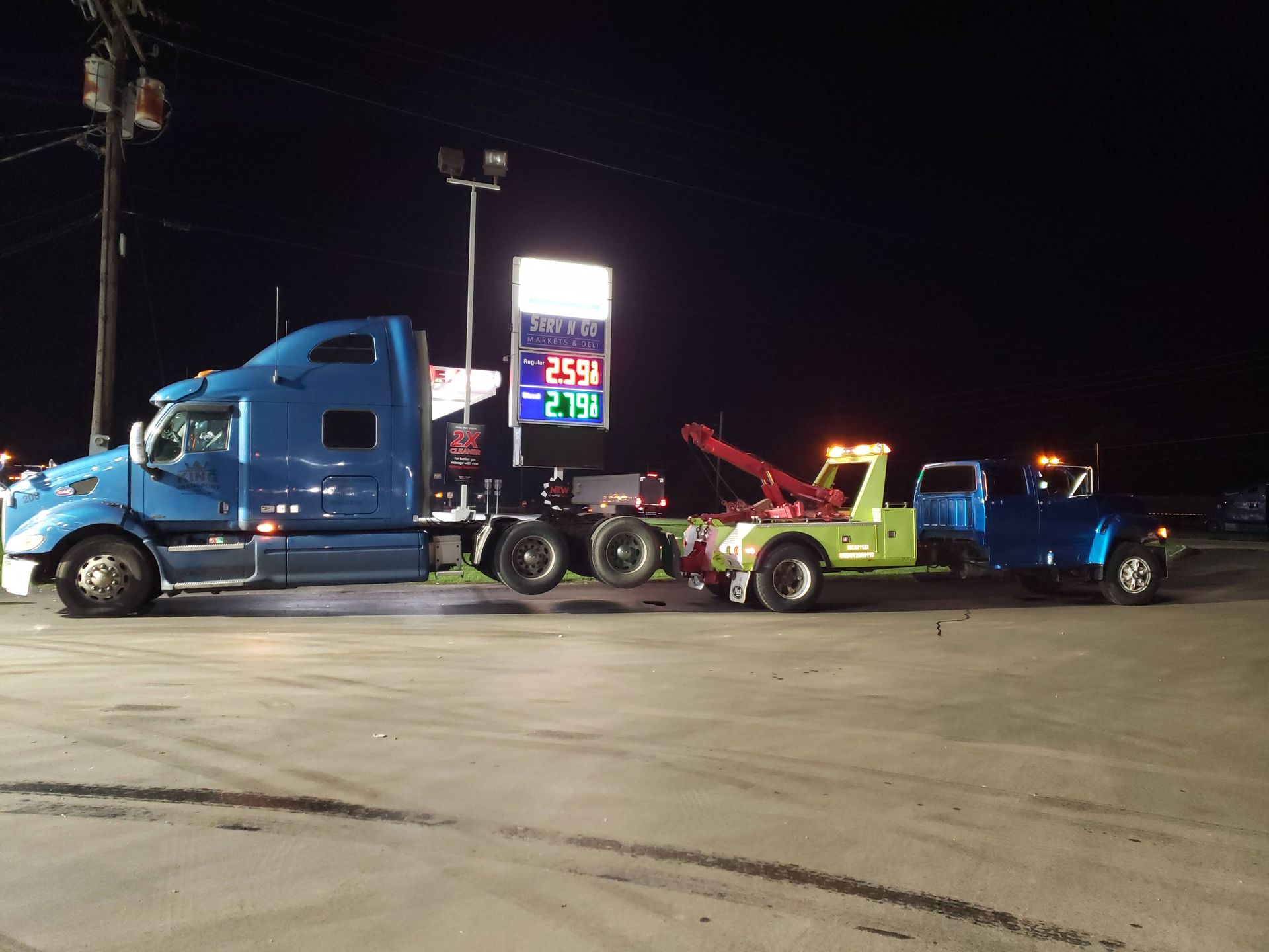A blue semi truck is being towed by a green tow truck.