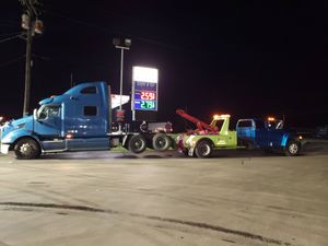 A blue semi truck is being towed by a green tow truck.