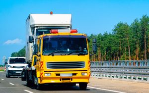 A yellow tow truck is driving down a highway next to a white truck.